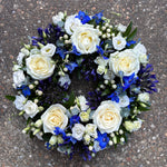 Load image into Gallery viewer, A circular floral wreath featuring white and cream roses, blue delphinium and green foliage
